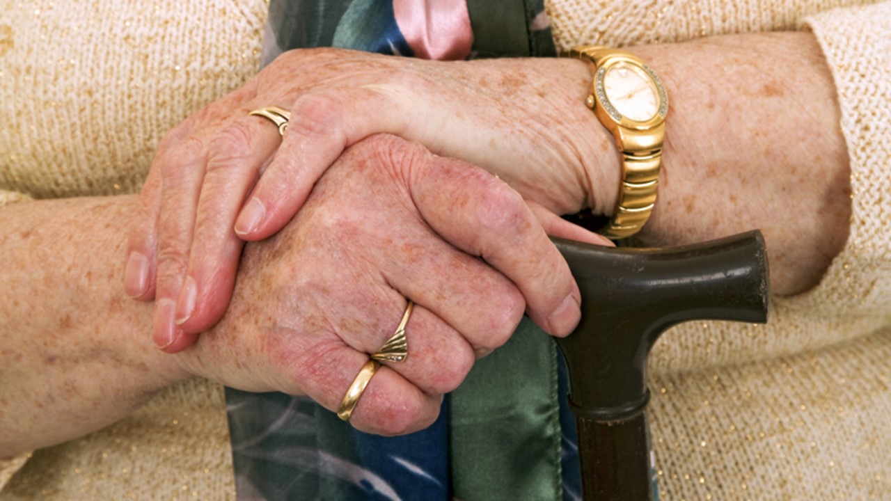 Bild som visar händerna på gammal person med käpp