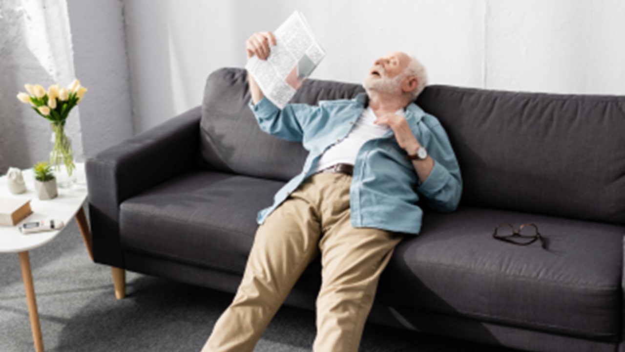Bild som visar äldre man i värmebölja som fläktar sig med en tidning